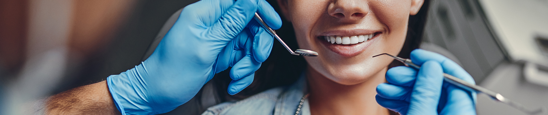 A woman sitting in a dental chair with a smiling expression, receiving dental care from a professional who is adjusting her braces.