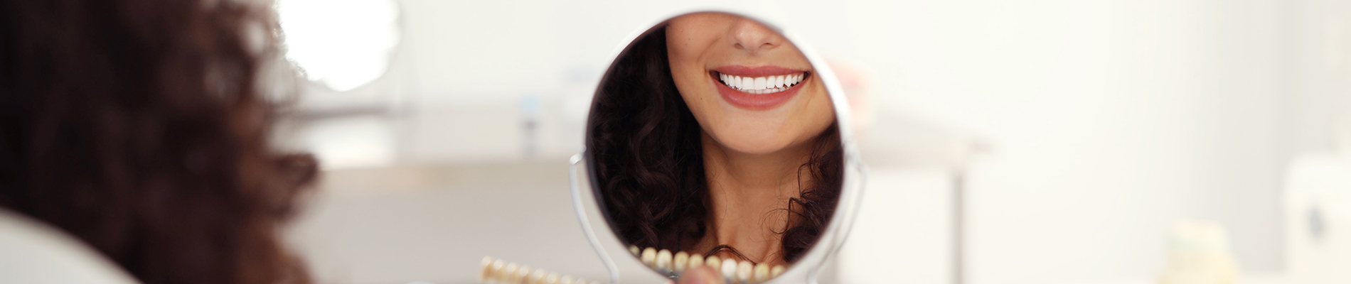 The image is a photograph of a woman with light skin, smiling at the camera. She appears to be in her late twenties or early thirties and has long hair. Her eyes are looking directly at the camera, and she is holding up her index finger near her mouth as if she s making a point or emphasizing something. The background is plain and light-colored, which suggests that this could be a stock photo used for various purposes such as advertising, personal branding, or lifestyle content.