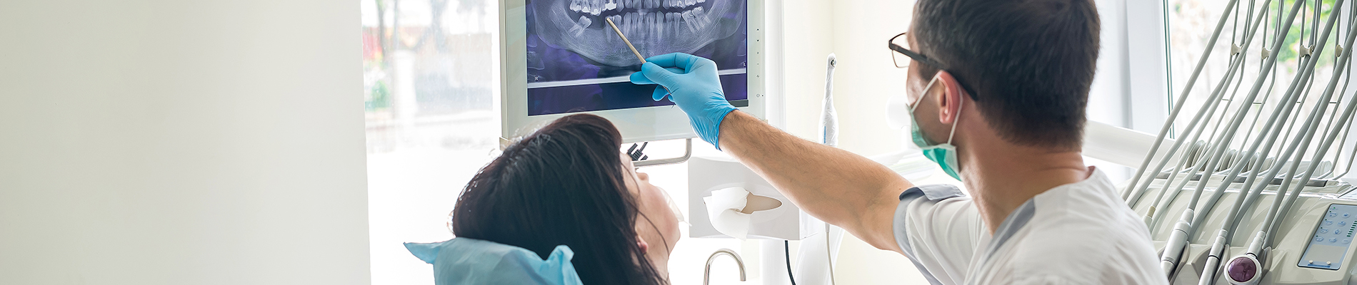 A healthcare professional in a white lab coat assisting another individual with a dental procedure, both wearing face masks and gloves.